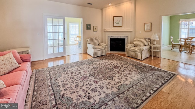 living room featuring a fireplace, a notable chandelier, visible vents, wood finished floors, and baseboards