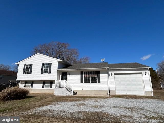 tri-level home featuring a garage and gravel driveway