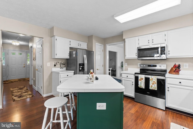 kitchen with dark wood-type flooring, a breakfast bar, white cabinetry, stainless steel appliances, and a center island