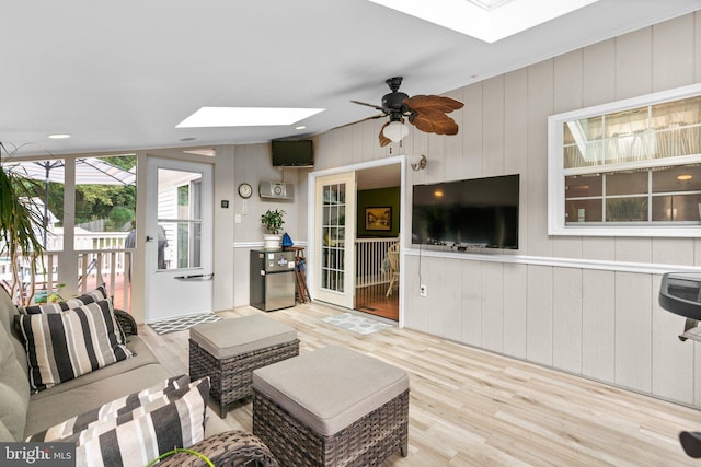 living room with ceiling fan, light hardwood / wood-style floors, and a skylight