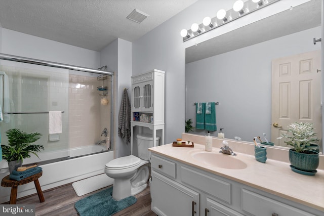 full bathroom featuring wood-type flooring, shower / bath combination with glass door, vanity, toilet, and a textured ceiling