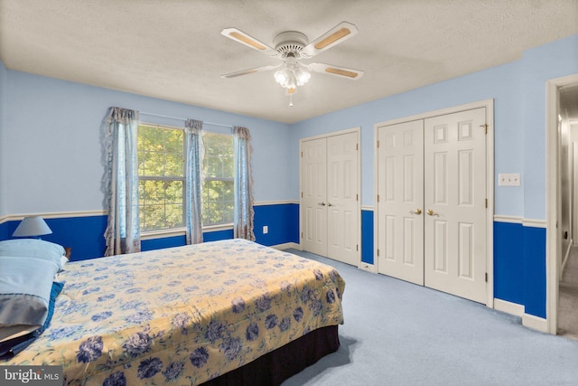 bedroom featuring ceiling fan, carpet flooring, a textured ceiling, and two closets