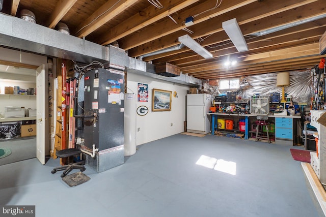 basement with white refrigerator, heating unit, and a workshop area