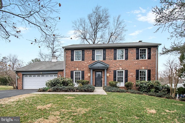 colonial inspired home with brick siding, aphalt driveway, a front yard, and an attached garage