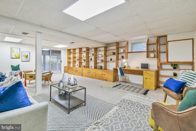 carpeted living room featuring visible vents, a paneled ceiling, and built in desk