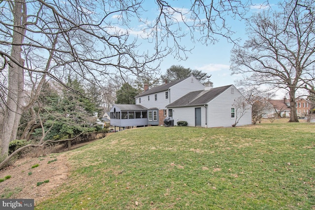 rear view of house featuring a yard, a sunroom, and a chimney