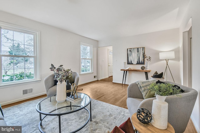 living area featuring visible vents, plenty of natural light, baseboards, and wood finished floors