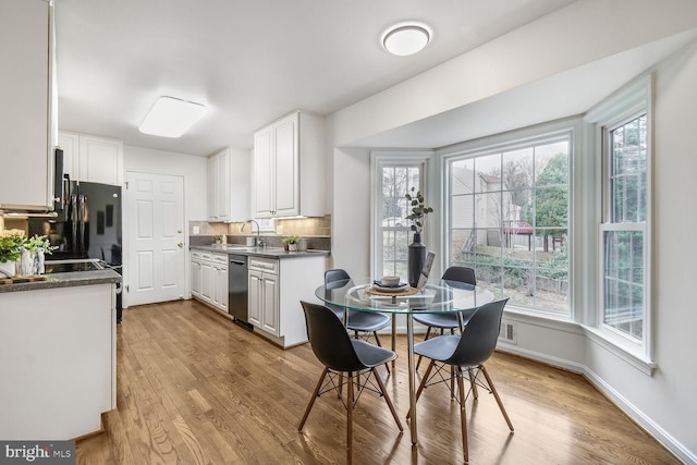 kitchen with baseboards, white cabinetry, decorative backsplash, light wood-style floors, and stainless steel dishwasher