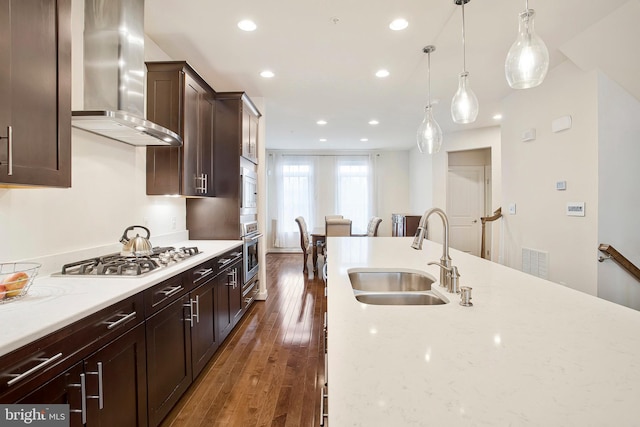 kitchen with light stone counters, gas cooktop, a sink, wall chimney range hood, and decorative light fixtures