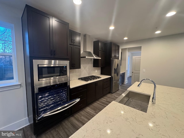 kitchen featuring wall chimney exhaust hood, appliances with stainless steel finishes, a sink, and light stone countertops