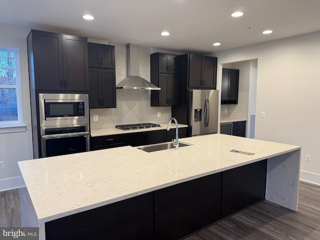 kitchen with wall chimney exhaust hood, a kitchen island with sink, stainless steel appliances, and a sink