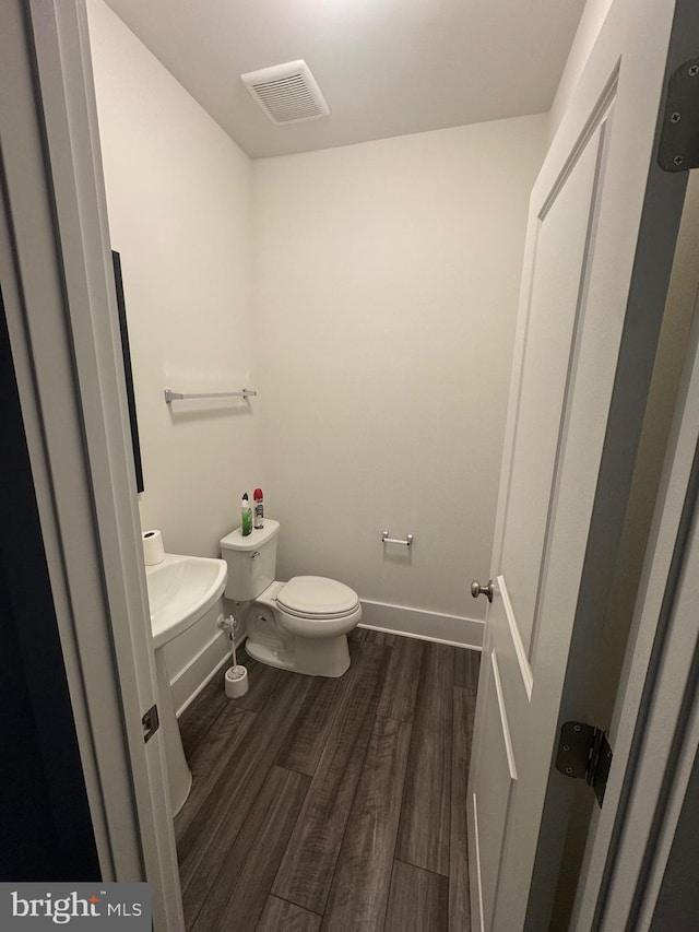 half bathroom with toilet, wood finished floors, visible vents, and baseboards