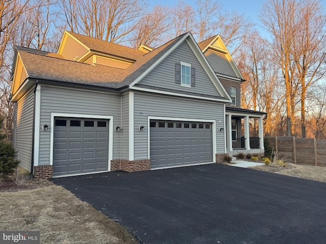 view of side of home with a garage, driveway, a shingled roof, and fence