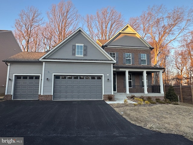 traditional-style home with an attached garage, covered porch, aphalt driveway, and brick siding