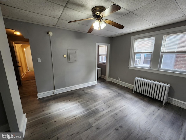 unfurnished room featuring ceiling fan, radiator heating unit, dark hardwood / wood-style floors, and a drop ceiling