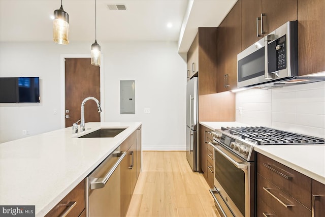 kitchen with sink, light hardwood / wood-style flooring, appliances with stainless steel finishes, pendant lighting, and decorative backsplash