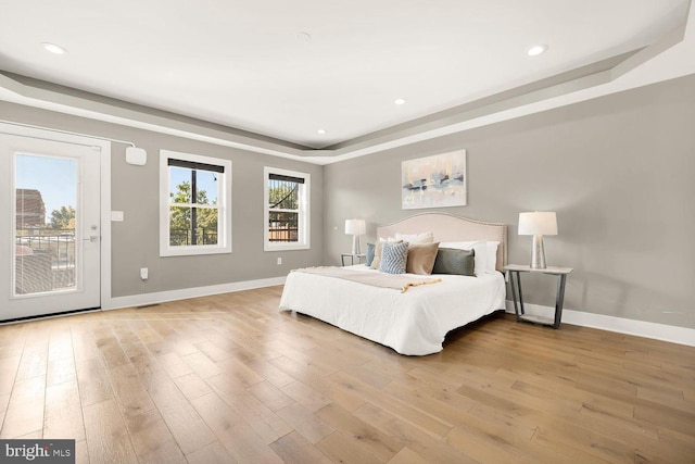 bedroom featuring a raised ceiling, access to exterior, and light wood-type flooring