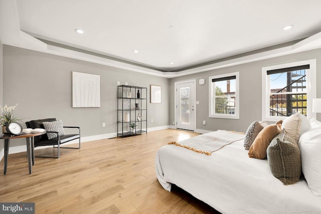 bedroom with access to exterior, a tray ceiling, and light wood-type flooring