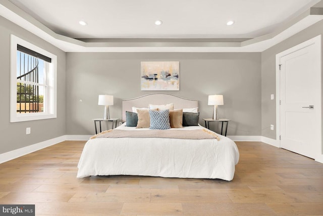 bedroom with light hardwood / wood-style floors and a tray ceiling