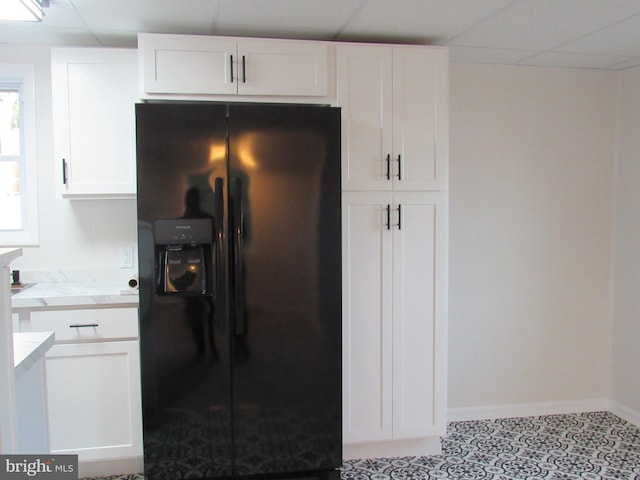 kitchen with baseboards, white cabinets, a drop ceiling, black fridge with ice dispenser, and light stone countertops