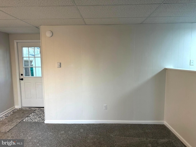 interior space featuring dark carpet, a paneled ceiling, and baseboards