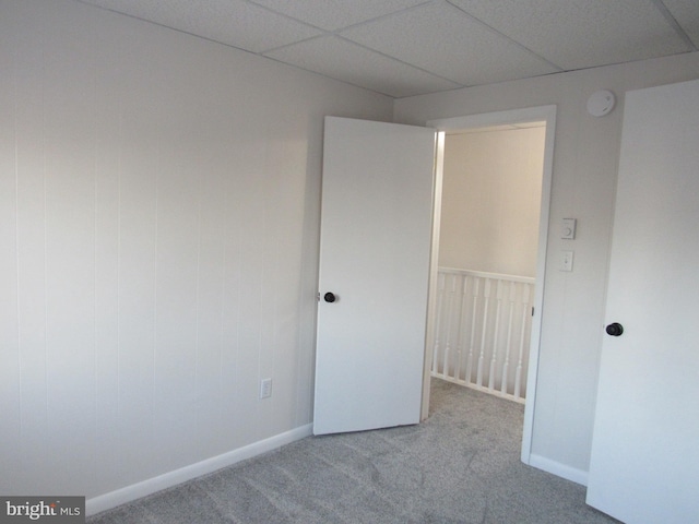 unfurnished bedroom featuring a drop ceiling, light carpet, and baseboards