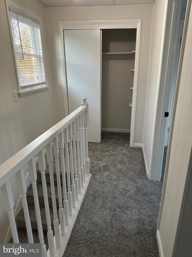 hallway featuring dark carpet and an upstairs landing