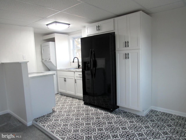 kitchen featuring stacked washer / dryer, a sink, black fridge with ice dispenser, white cabinetry, and light countertops