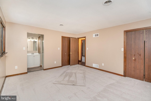 unfurnished bedroom featuring multiple closets, light colored carpet, and ensuite bathroom