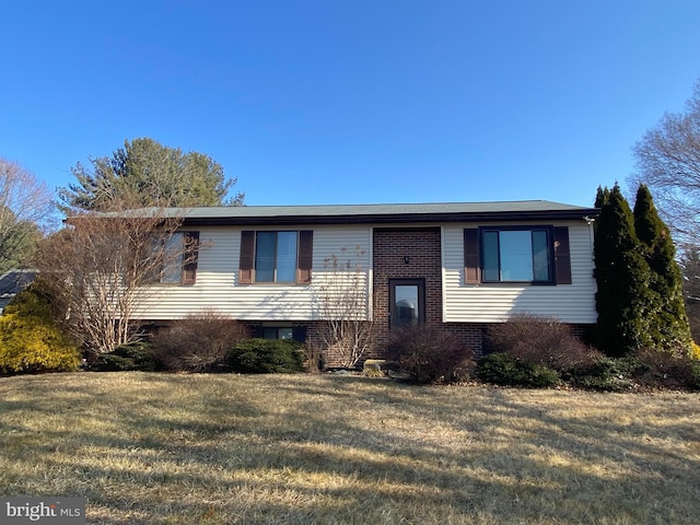 raised ranch featuring brick siding and a front lawn