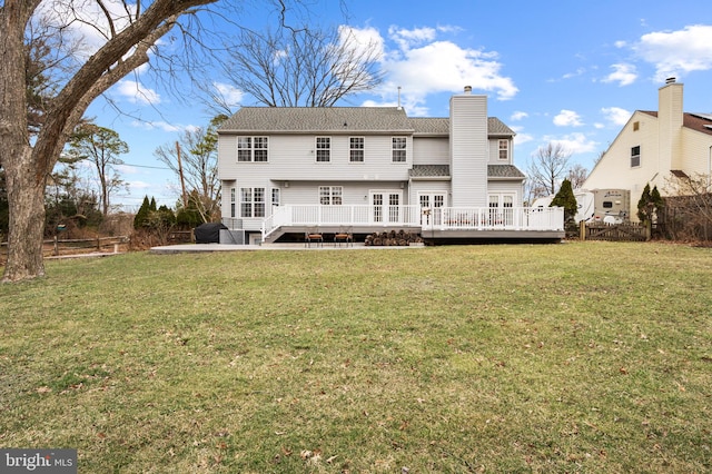 rear view of house with a deck, a yard, a chimney, and fence