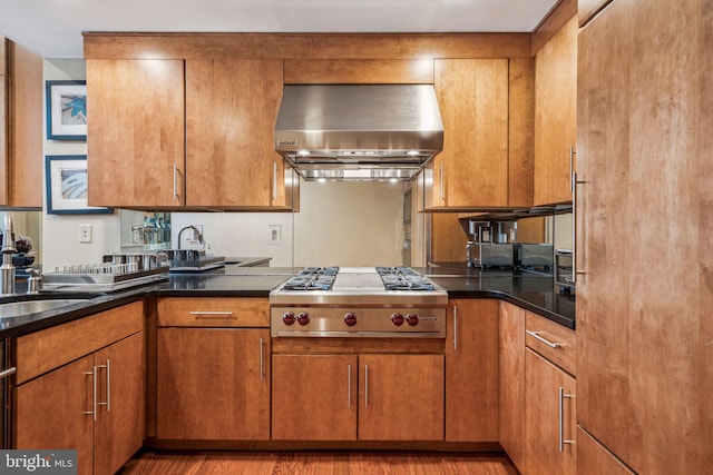 kitchen with light wood-style floors, wall chimney exhaust hood, stainless steel gas cooktop, and brown cabinets