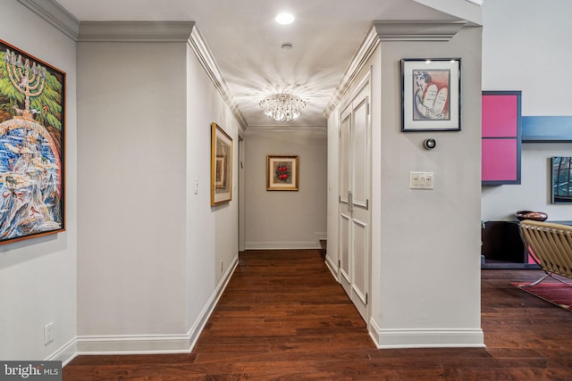 corridor with ornamental molding, a notable chandelier, baseboards, and wood finished floors