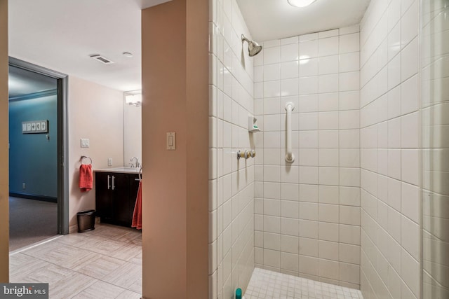 bathroom with tiled shower, vanity, visible vents, and baseboards