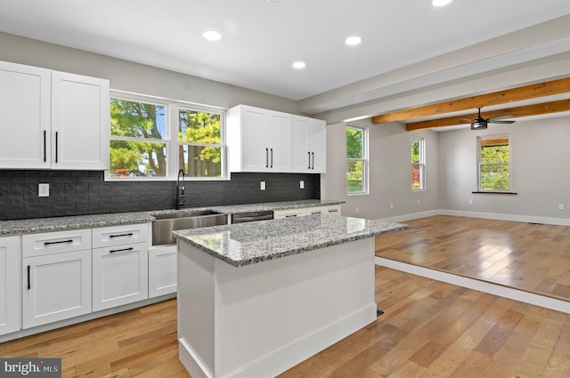 kitchen with sink, white cabinetry, a center island, tasteful backsplash, and light stone countertops