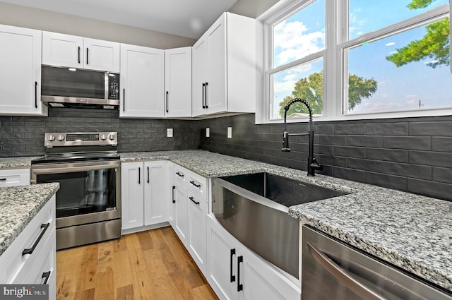 kitchen with light stone counters, stainless steel appliances, sink, and white cabinets