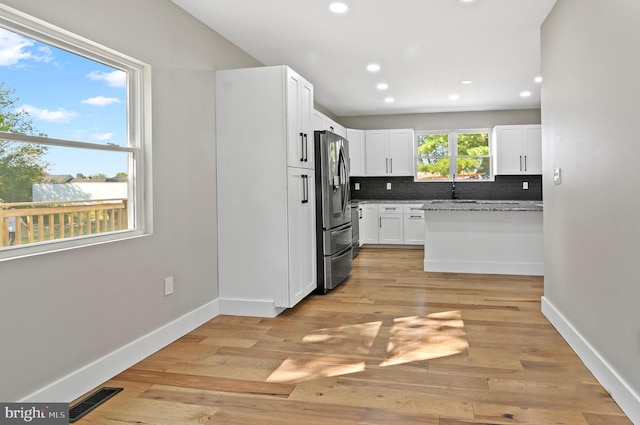 kitchen featuring white cabinetry, backsplash, light stone counters, stainless steel fridge with ice dispenser, and light wood-type flooring