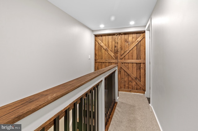 hallway featuring light colored carpet and a barn door