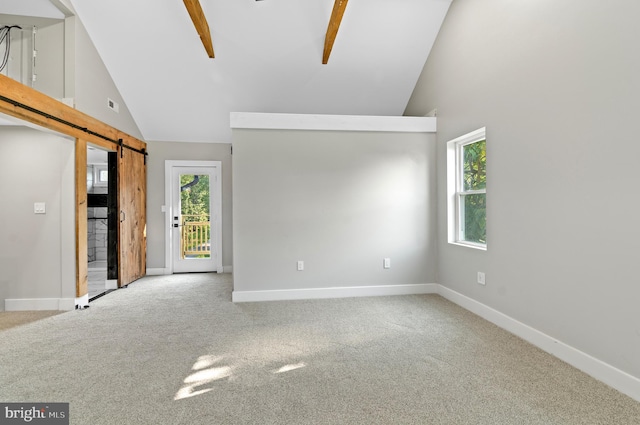 carpeted empty room with a barn door and high vaulted ceiling