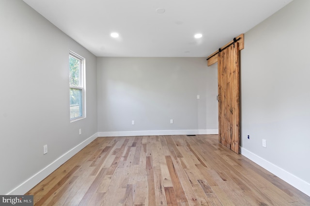 unfurnished room with a barn door and light wood-type flooring