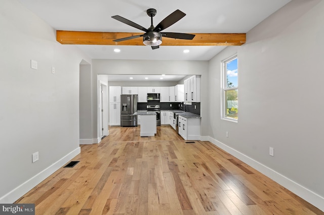 kitchen with stainless steel appliances, beamed ceiling, white cabinets, and decorative backsplash