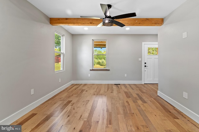 spare room with beamed ceiling, plenty of natural light, and light wood-type flooring