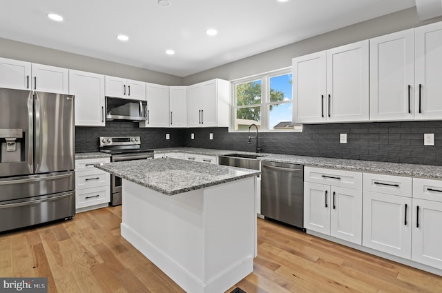 kitchen with sink, stainless steel appliances, light stone countertops, white cabinets, and a kitchen island