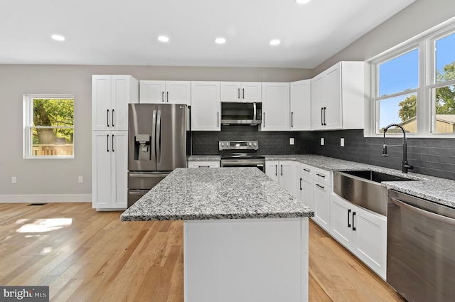 kitchen with a center island, appliances with stainless steel finishes, light stone countertops, and sink