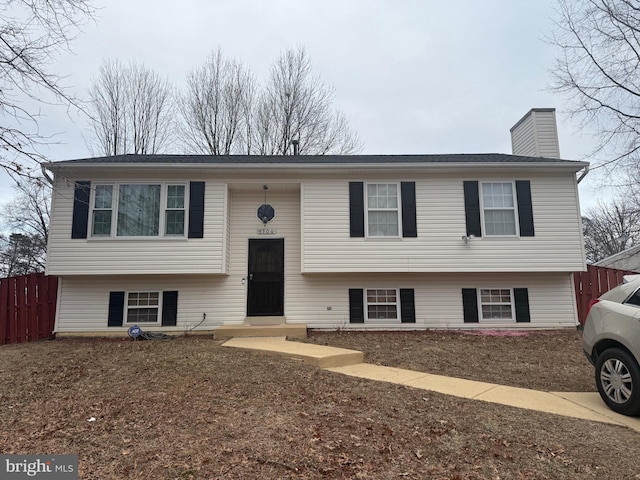 bi-level home with entry steps, fence, and a chimney