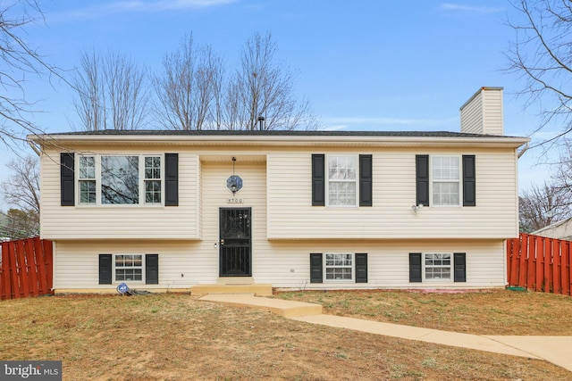 raised ranch with a front yard, fence, and a chimney