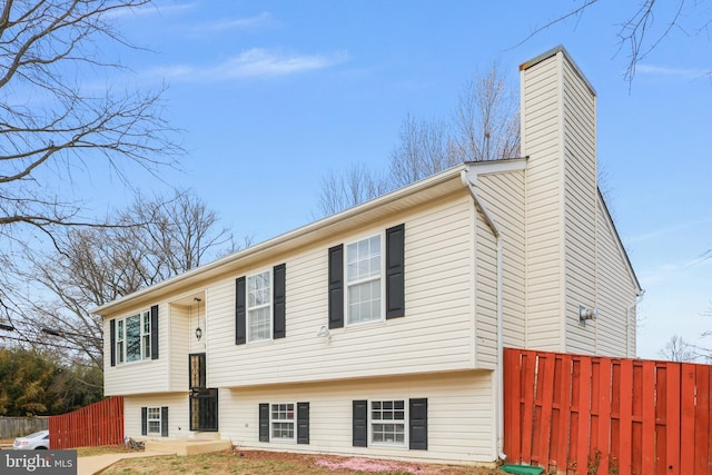 bi-level home with a chimney and fence