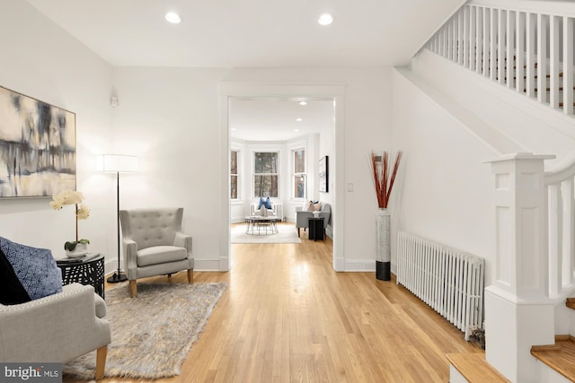 living area featuring radiator, light wood-type flooring, stairs, and recessed lighting