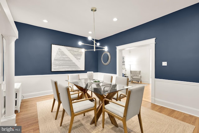 dining area with a wainscoted wall, light wood-style flooring, an inviting chandelier, ornate columns, and recessed lighting