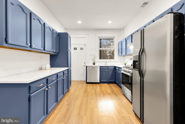 kitchen featuring light wood finished floors, visible vents, blue cabinets, stainless steel appliances, and light countertops